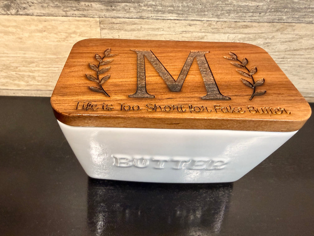 Butter dish with wooden lid featuring engraved letter and text.